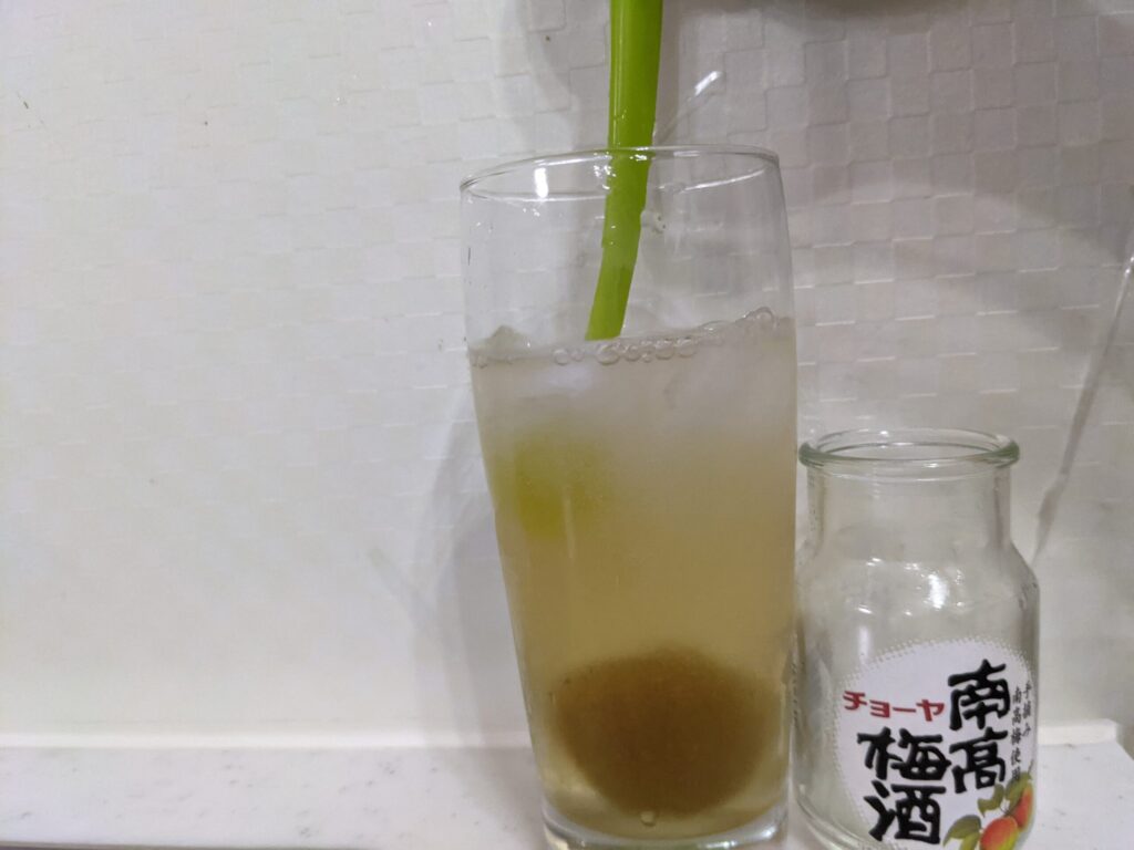「チョーヤ南高梅酒（梅入り）95mlの炭酸水割り」が入ったグラス内をスプーンでかき混ぜているところ